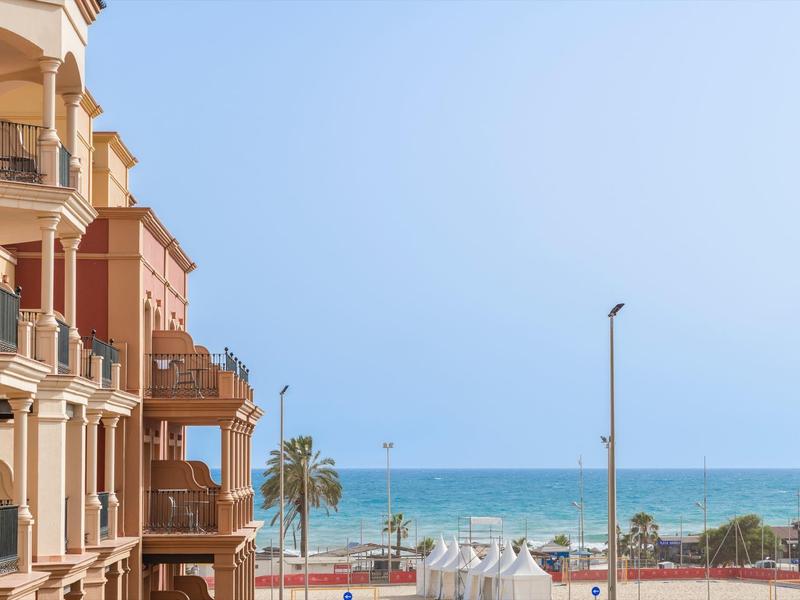 Mehrstöckige Gebäude am Strand mit blauem Himmel und ruhigem Meer im Hintergrund.