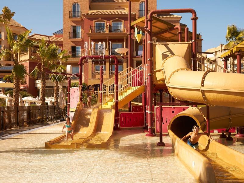 Bunter Wasserspielplatz mit Rutschen und Wasserbecken unter blauem Himmel bei Hotel.