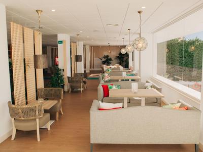 Helles Café mit großen Fenstern, moderner Holz- und Weiß-Dekor, gedeckten Sofas und Gewebesesseln.