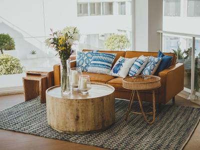 Gemütliche Sitzecke mit brauem Sofa, bunten Kissen und rundem Holztisch auf Teppich im hellen Raum.