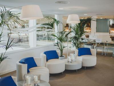 Modern eingerichteter Lounge-Bereich mit weißen Sesseln, blauen Kissen und Pflanzen.