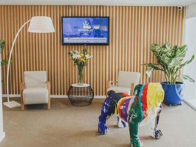 Moderne Hotellobby mit buntem Hundefigur, gemütlichen Sesseln und Pflanzen vor Holzpaneelwand.