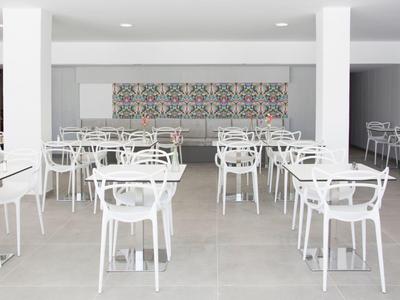 Moderner Speiseraum mit weißen Tischen und Stühlen auf grauem Boden und dekorativem Wandmuster.