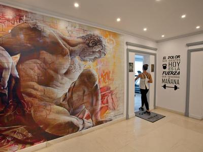 Ein Flur mit einem großen Wandgemälde eines athletischen Mannes und einer motivierenden spanischen Wandinschrift.