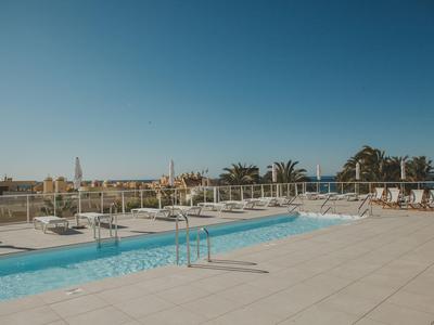 Moderner Außenpool mit Liegestühlen und Geländer unter klarem blauem Himmel.