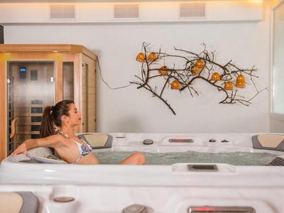 Frau entspannt in einem modernen Whirlpool mit Wanddekoration aus Ästen und orangen Kugeln.