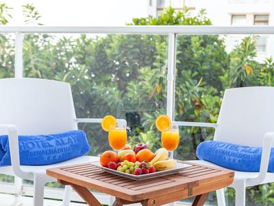 Balkon mit zwei weißen Stühlen, blauen Kissen, Holz-Tisch und Obstteller mit Orangensaftgläsern.