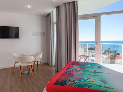 Camera d'hotel luminosa con vista sul mare, mobili moderni e terrazza con sedie.