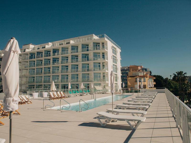 Moderner Hotelpoolbereich mit Liegestühlen und Sonnenschirmen unter klarem Himmel.