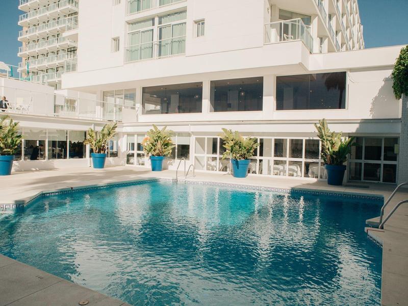 Moderner Außenpool mit blauem Wasser, umgeben von weißem Gebäude und blauen Pflanzgefäßen.