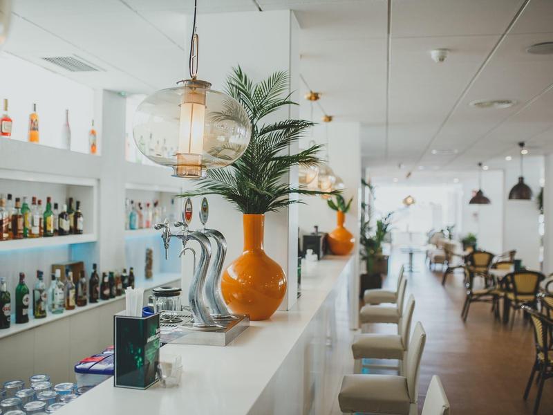 Moderne Bar mit hellen Wänden, großen Spiegeln, orangefarbenen Vasen und gemütlichen Sitzplätzen.