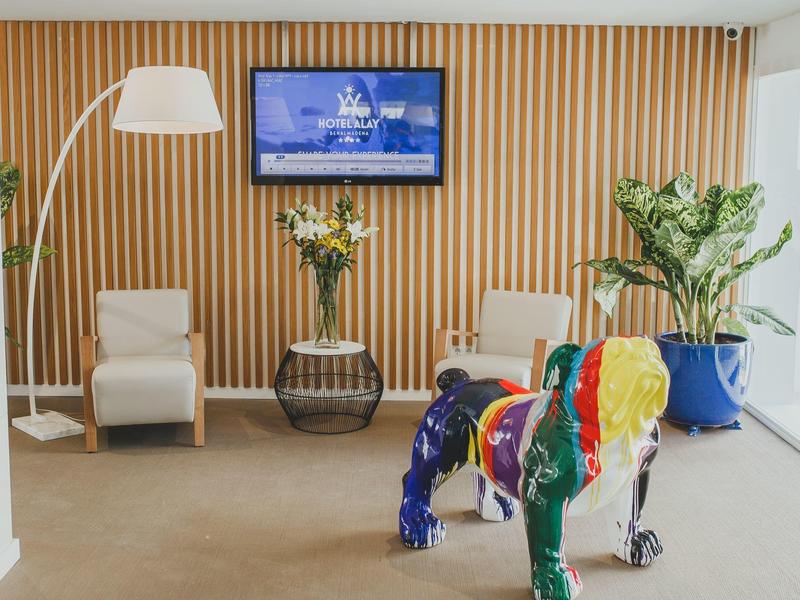 Moderne Hotellobby mit buntem Hundefigur, gemütlichen Sesseln und Pflanzen vor Holzpaneelwand.