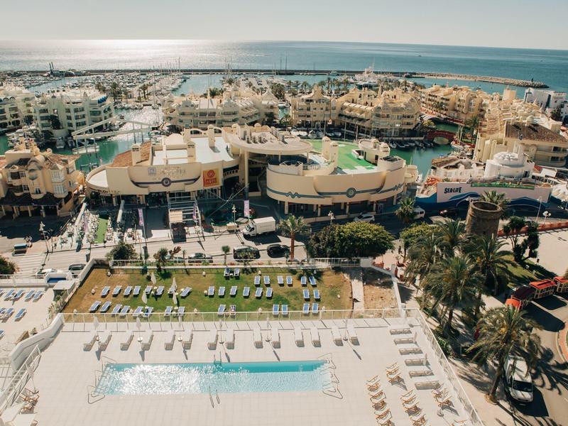 Großes Resort mit Pool, Liegestühlen, Palmen, Gebäuden und Blick auf das Meer im Hintergrund.