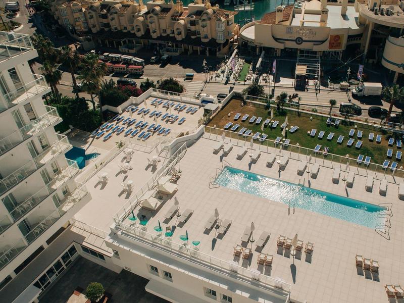 Großer Hotelpool mit Liegestühlen und Palmen in hellem, sonnigem Außenbereich.