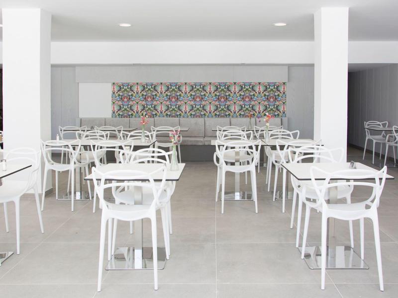 Moderner Speiseraum mit weißen Tischen und Stühlen auf grauem Boden und dekorativem Wandmuster.