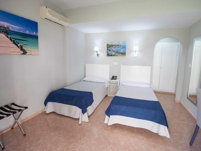 Zimmer mit zwei Einzelbetten, blauen Decken, weißen Wänden und Landschaftsbildern.