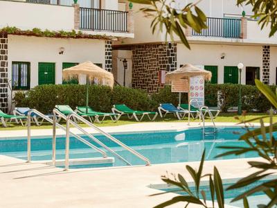 Ein Pool mit Liegestühlen, Sonnenschirmen und einer zweistöckigen Hotelwand im Hintergrund.
