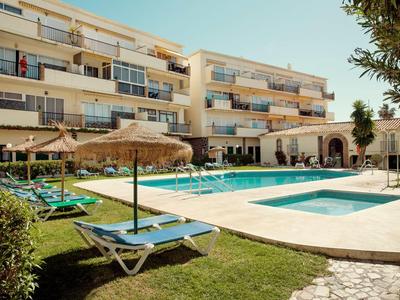 Moderner mehrstöckiger Gebäudekomplex mit Pool, Sonnenliegen und Schirmen bei sonnigem Wetter.