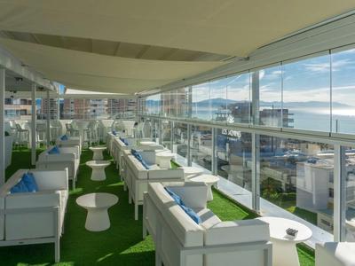 Moderne Dachterrasse mit weißen Sitzmöbeln, Glastüren und Meerblick bei Tageslicht.