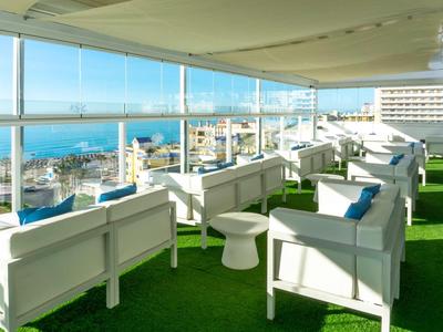 Offene Dachterrasse mit weißen Sitzmöbeln und grünem Kunstrasen mit Aussicht aufs Meer.