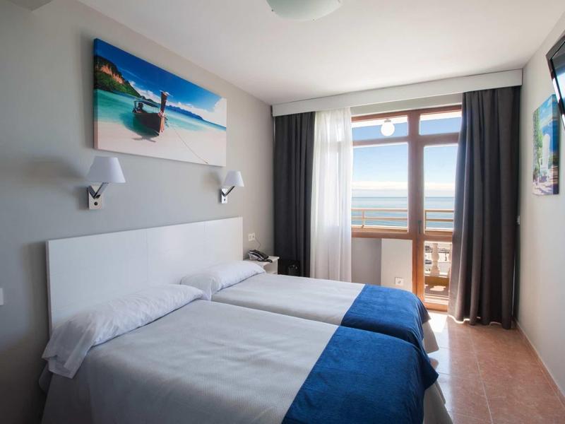 Zweibettzimmer mit weißen Wänden, blauen Decken, großem Fenster und Blick aufs Meer.