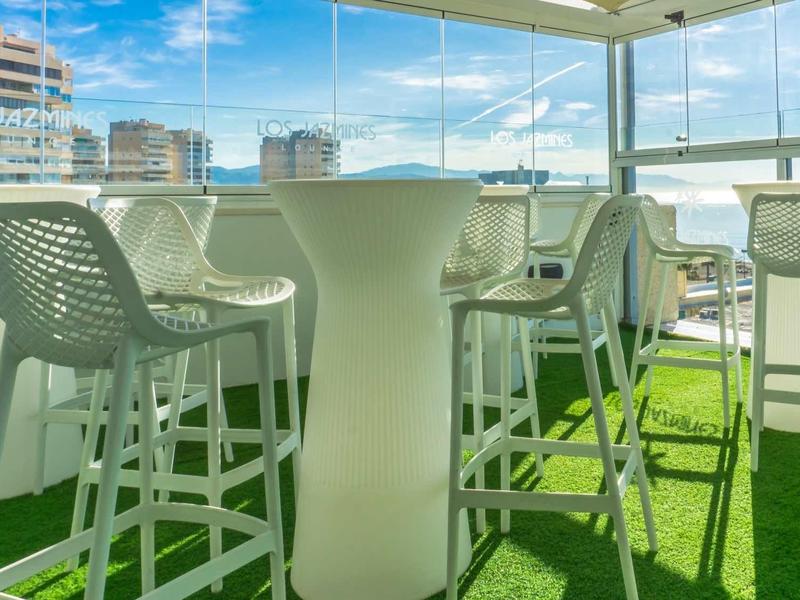 Moderner Dachterrassenbereich mit weißen Barhockern, Stehtischen und grünem Kunstrasenboden.