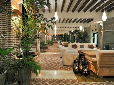 Wnętrze holu z drewnianymi belkami sufitowymi, roślinami i przytulnymi miejscami do siedzenia.