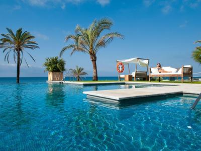 Infinity-Pool mit klar blauem Wasser, Palmen und Sonnenliegen unter strahlend blauem Himmel.