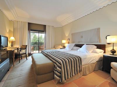 Geräumiges Schlafzimmer mit großem Bett, gestreifter Decke, Nachttischen und Balkon mit Blick nach draußen.