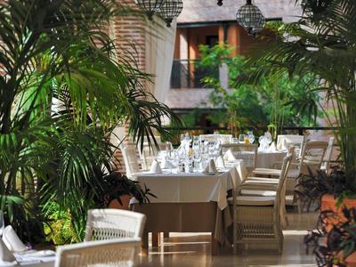 Restaurantterrasse mit weißen Tischen und Stühlen, umgeben von grünen Pflanzen und natürlichem Licht.