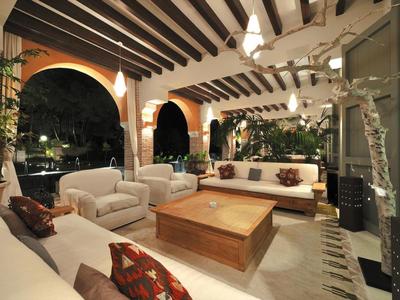 Große überdachte Terrasse mit weißem Polstermöbeln, Holztisch, Bogenfenstern und offener Decke aus Holzbalken.