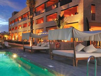 Modernes Hotel mit beleuchtetem Pool, Liegen und warmem Licht bei Abenddämmerung.