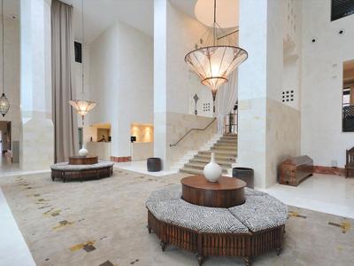 Jasna lobby hotelowa z okrągłymi miejscami do siedzenia, schodami i dużymi żyrandolami.