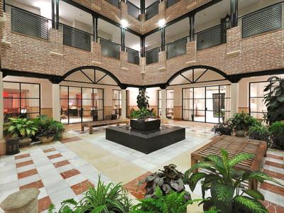 Innenhof mit Pflanzbeeten, quadratischem Brunnen, roten Backsteinwänden und großen Fenstern.