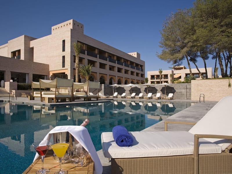 Moderner Hotelpool mit weißen Liegen, blauen Handtüchern und mehreren Cocktails auf kleinem Tisch.