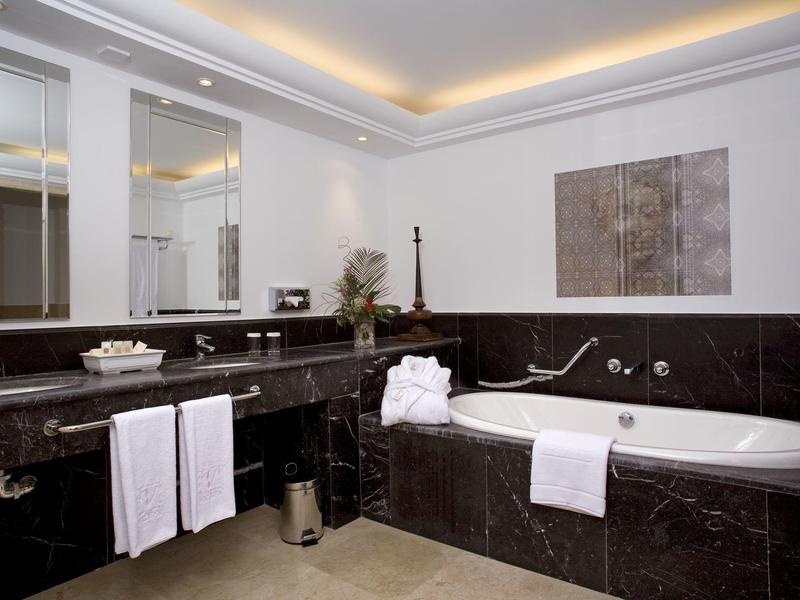 Helles Badezimmer mit schwarzer Marmorwanne, großem Spiegel, weißem Handtuch und moderner Deckenbeleuchtung.