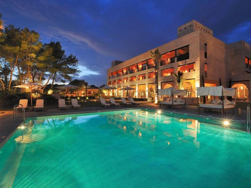 Beleuchteter Hotelpool mit klarem Wasser vor einem großen, modernen Gebäude in der Abenddämmerung.