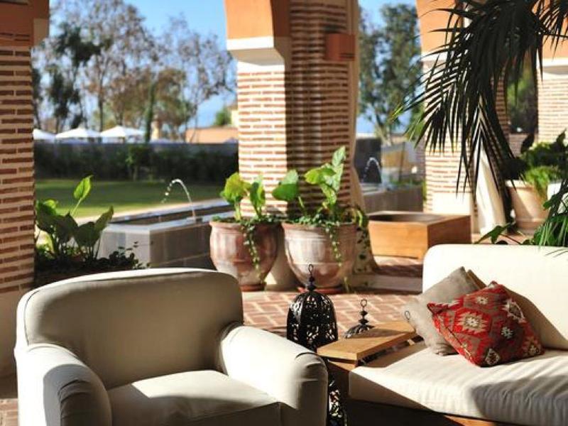 Gemütliche Terrasse mit weißen Sesseln, Pflanzen, Backsteinbögen und Blick aufs Meer.