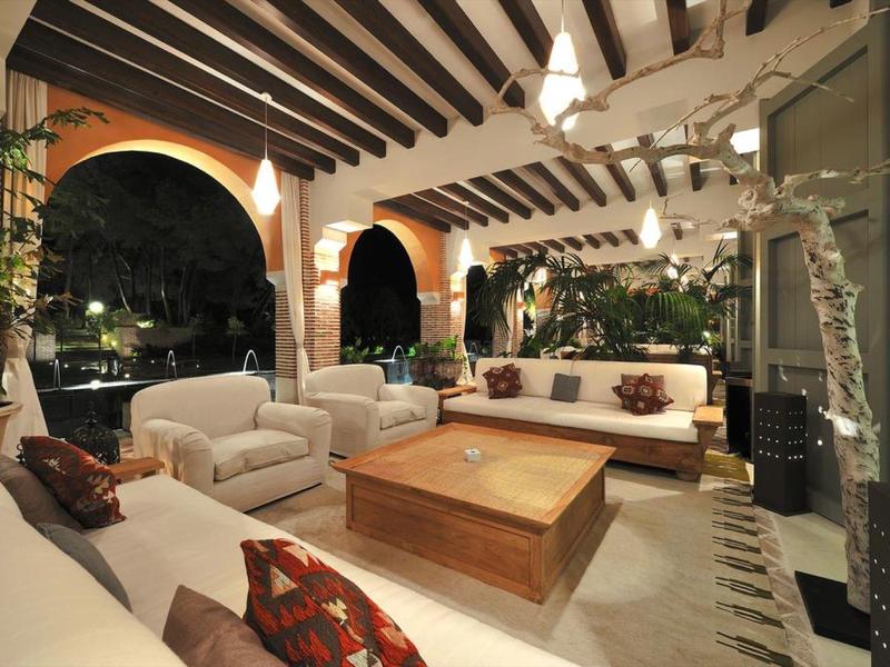 Große überdachte Terrasse mit weißem Polstermöbeln, Holztisch, Bogenfenstern und offener Decke aus Holzbalken.