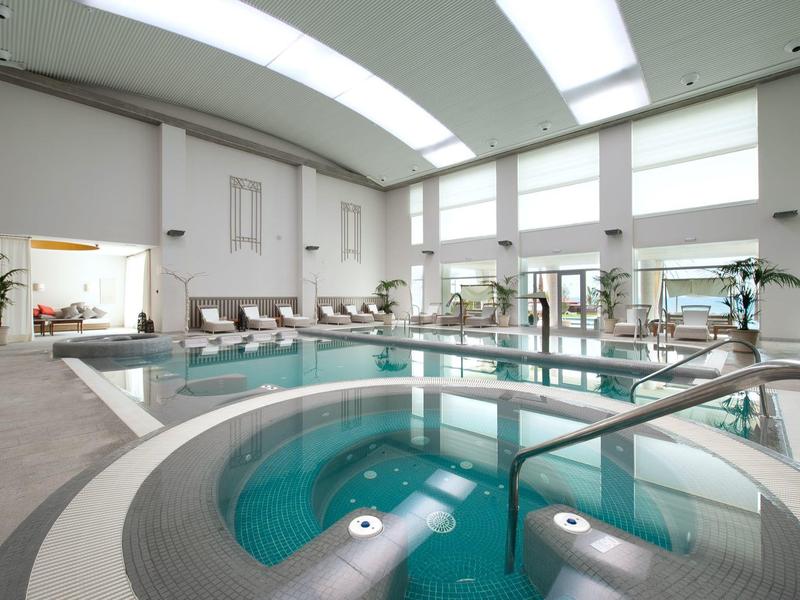 Moderne Wellness-Oase mit rundem Whirlpool und großem Schwimmbad in hellem Raum.