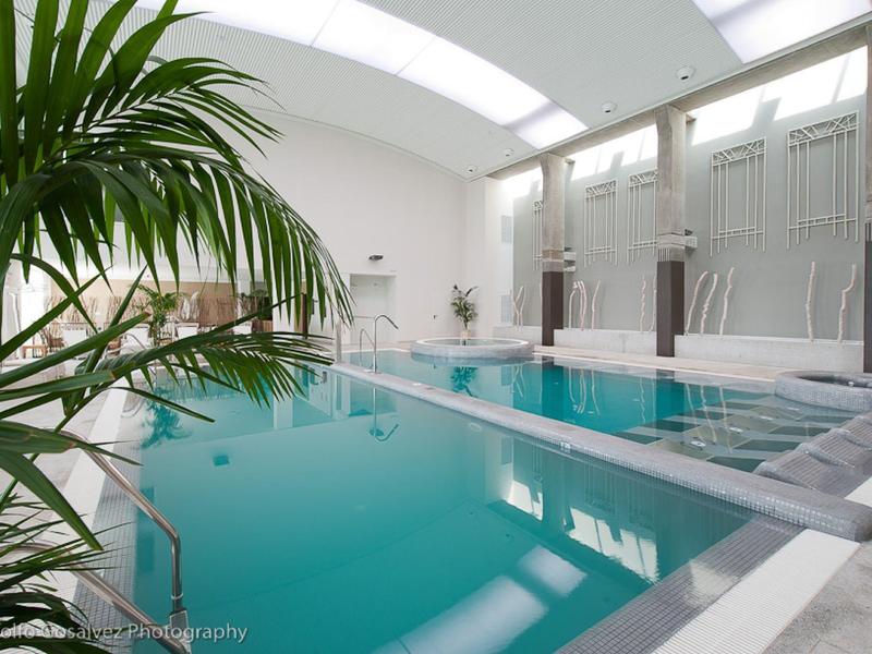 Moderner Innenpool mit türkisblauem Wasser, weißen Wänden, großen Fenstern und grünen Pflanzen.