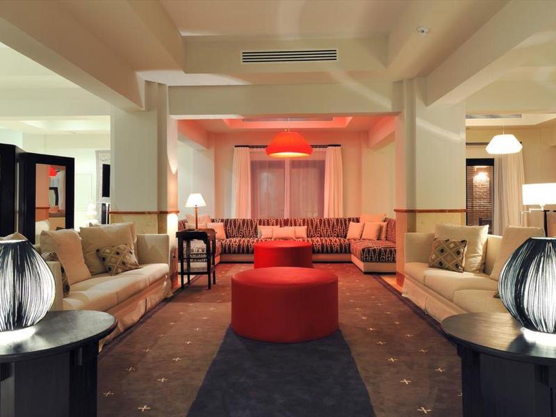 Großer Wohnraum mit beigen Sofas, runden roten Hockern und dekorativen Lampen auf schwarzen Tischen.