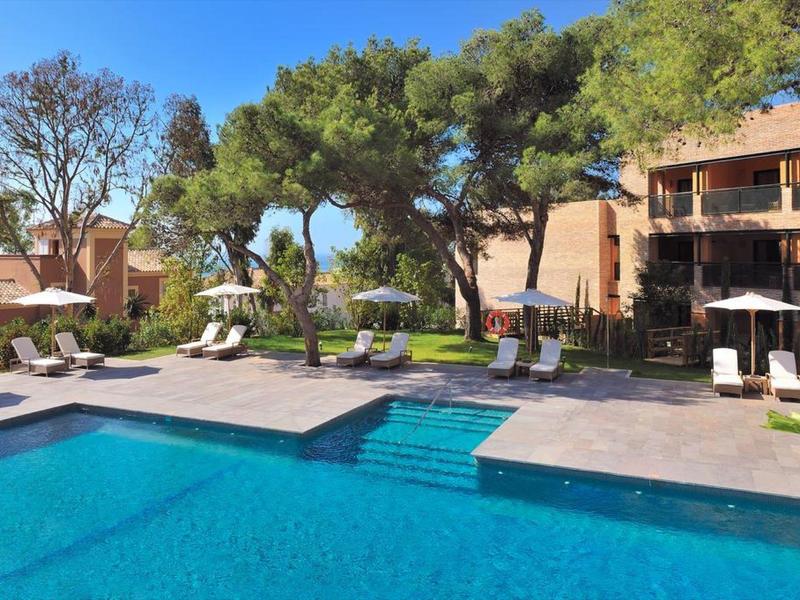 Moderner Außenpool mit blauer Wasserfläche, umgeben von Liegestühlen, Bäumen und Gebäuden.