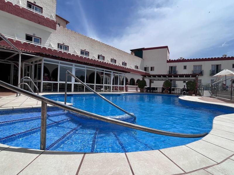 Freier Pool mit Edelstahlgeländer, roten Dächern und weißem Fliesenboden unter blauem Himmel.