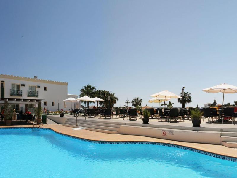 Großer blauer Pool mit runder Form neben Gebäude und Terrasse mit Sonnenstühlen und Schirmen.