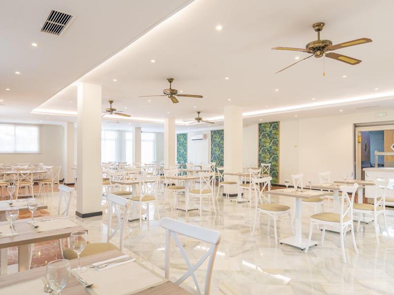 Helles, modernes Restaurant mit weißen Möbeln, großen Fenstern und Deckenventilatoren.