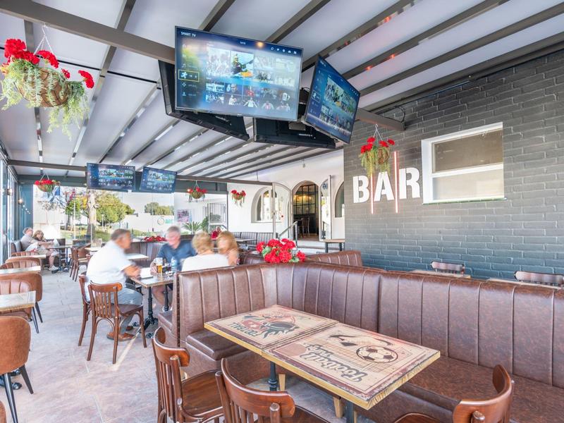 Modernes Café mit dunklem Ledersofa, Holztischen, Hängemarken und mehreren Fernsehern an der Wand.