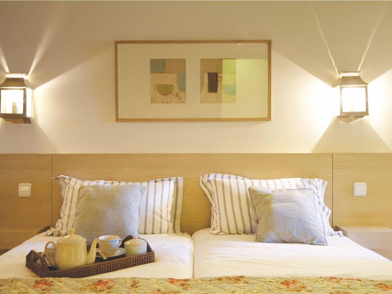 Hell eingerichtetes Schlafzimmer mit zwei Betten, gestreiften Kissen und warmem Wandlicht.