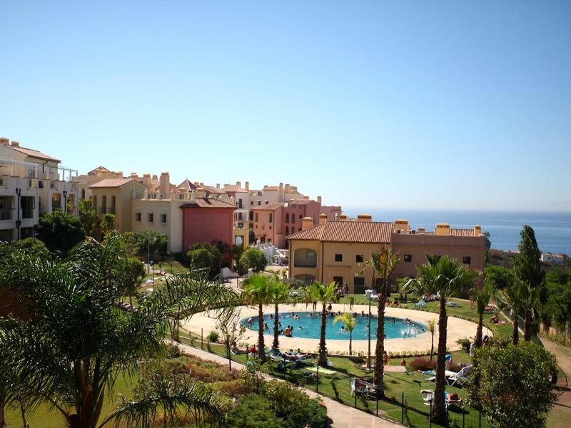 Wohnanlagen mit Pools, Palmen und blauem Himmel am Meer in einer sonnigen, mediterranen Landschaft.
