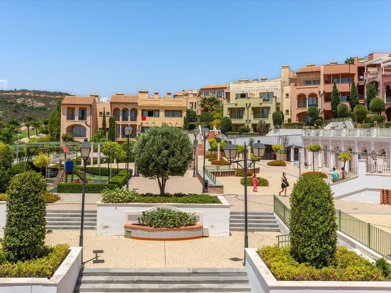 Moderner Wohnkomplex mit bunten Gebäuden, grünen Pflanzen und klar blauem Himmel im Hintergrund.